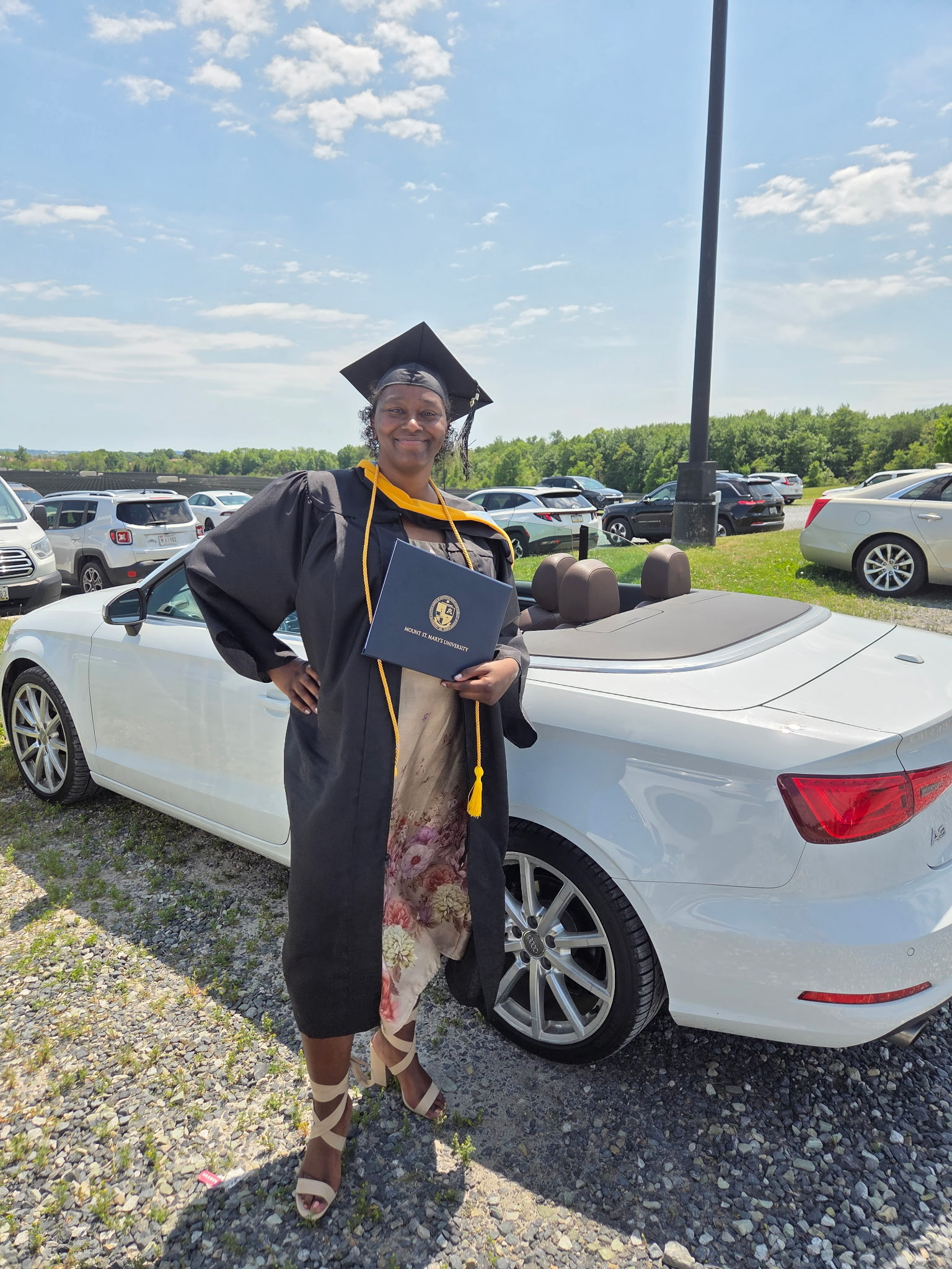 Talisha, receptora de un trasplante de hígado, posa junto a un coche con toga y birrete tras graduarse en la Universidad Mount St. Mary con una licenciatura en Ciencias.