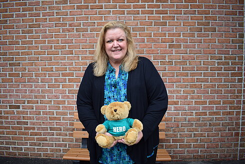 Director, Compensation and Benefits, Leslie Reed, is smiling while she holds a hero heart teddy bear in support of organ, eye and tissue donation in front of Infinite Legacy's office.