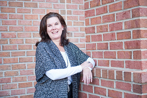 Executive Vice President and Chief Operations Officer, Debbie Williams, leaning against a brick wall outside of Infinite Legacy's office.