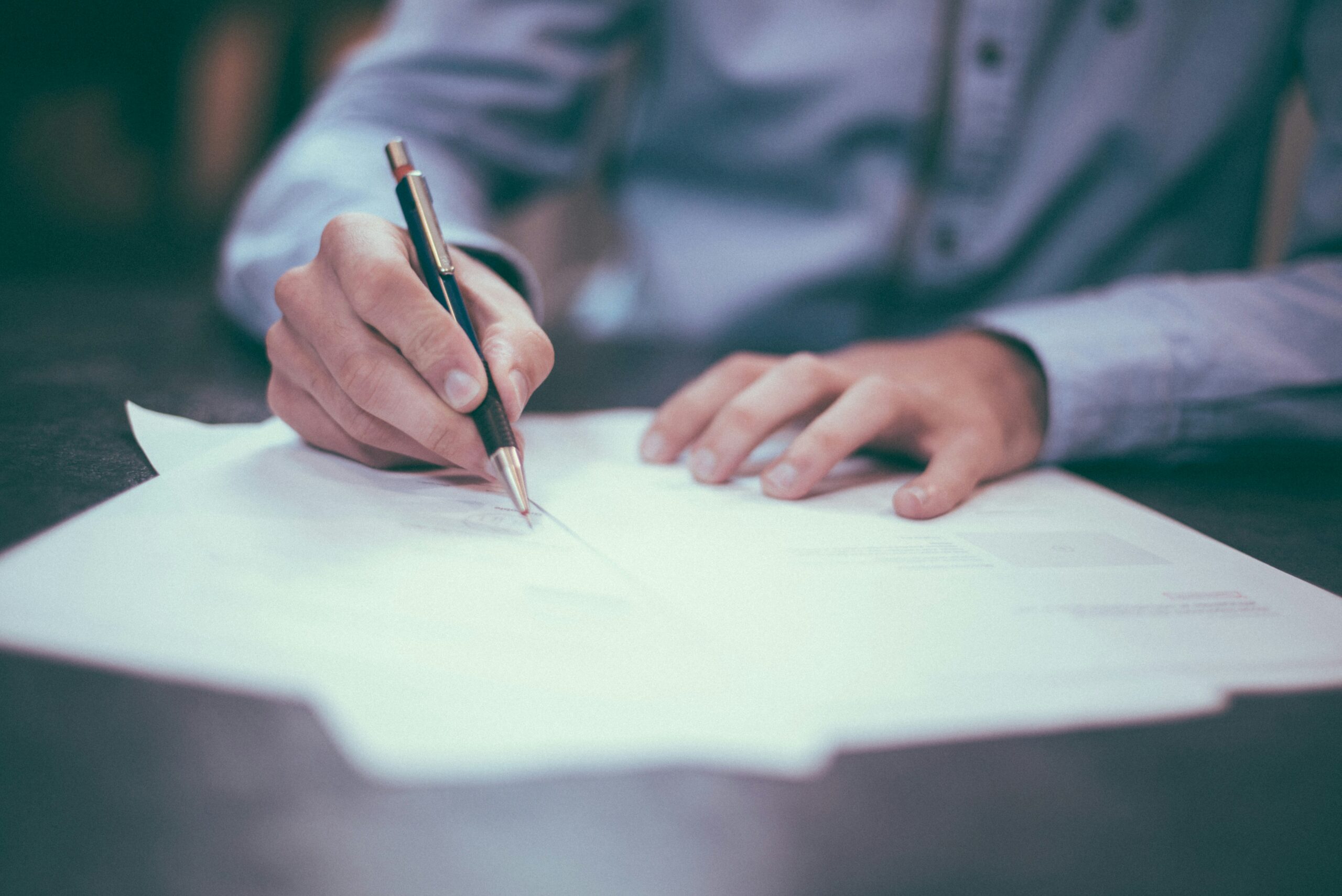 A person holding a pen and signing a document.