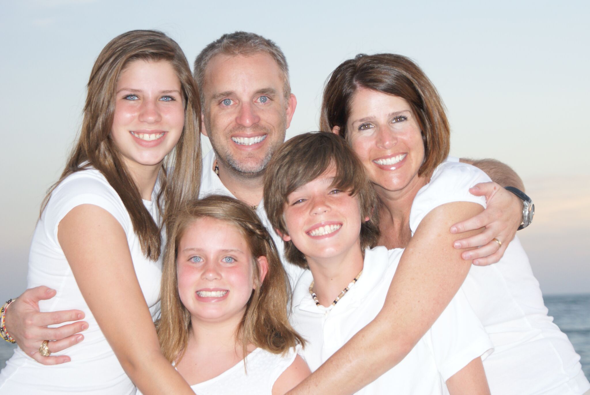 Taylor with her family, including her dad, mom, brother and sister wear white shirts at the beach.