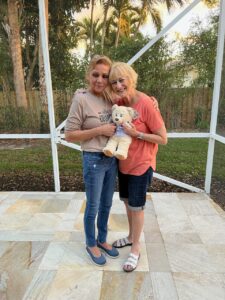 Carmen Blake and Phyllis Weissblum wrap their arms around each other, holding a teddy bear.