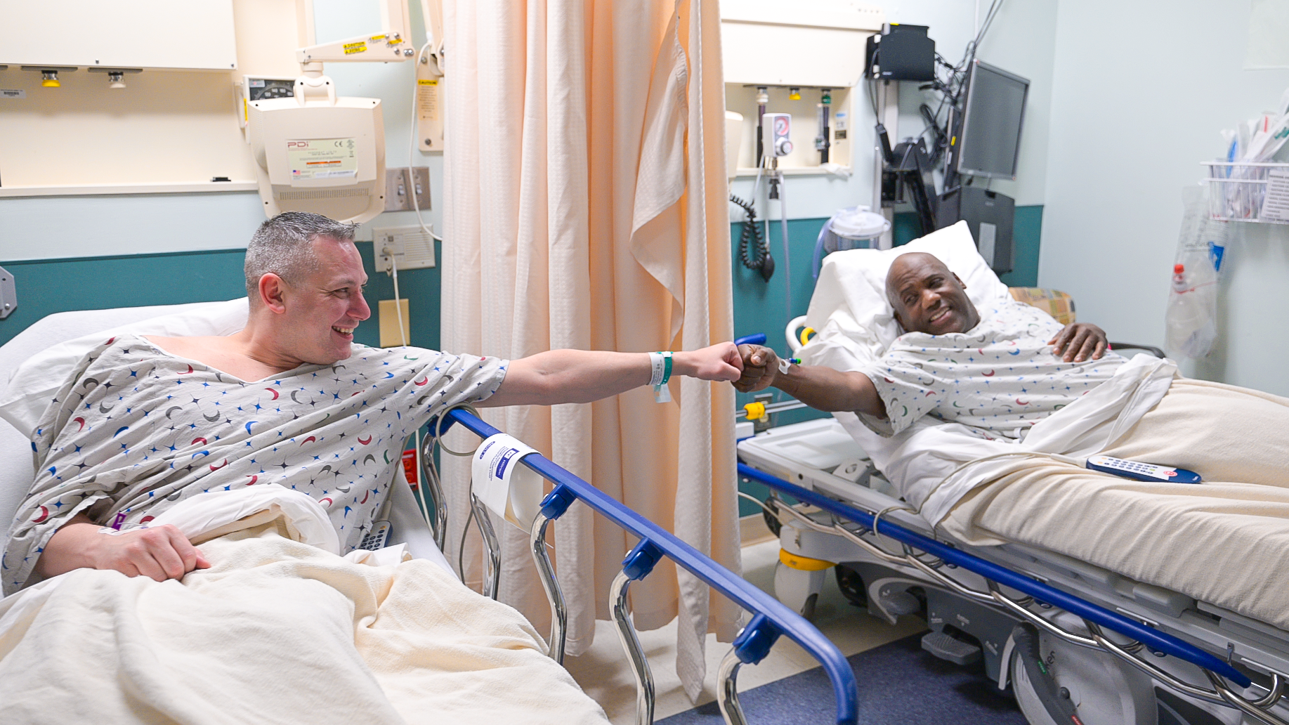 James Harris and Russ Redhead fist bump in their hospital beds before going into surgery.