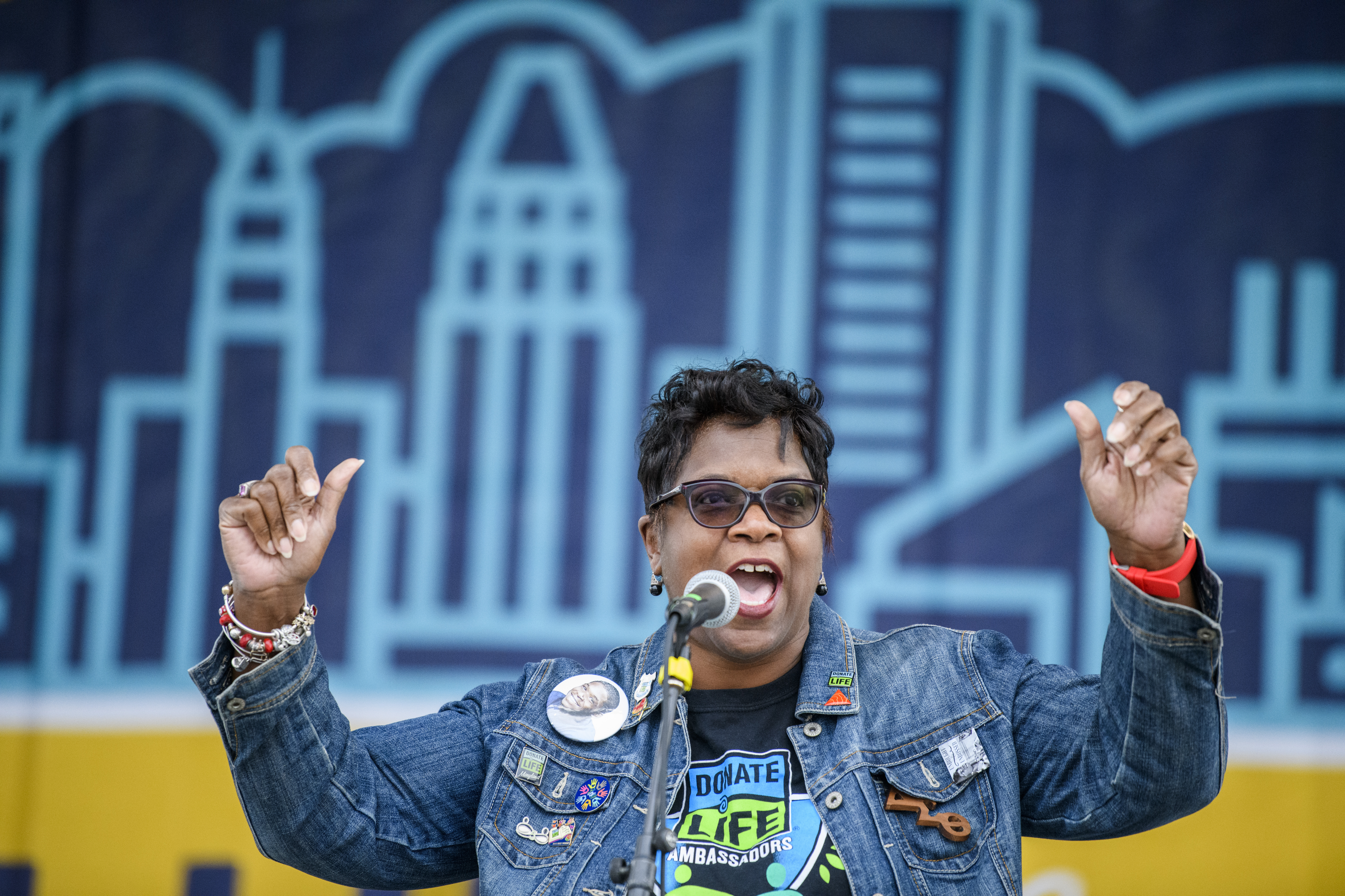 A woman presents on stage at the Annual Donate Life Family Fun Run wearing a Donate Life Ambassador t shirt and Donate Life label pins.
