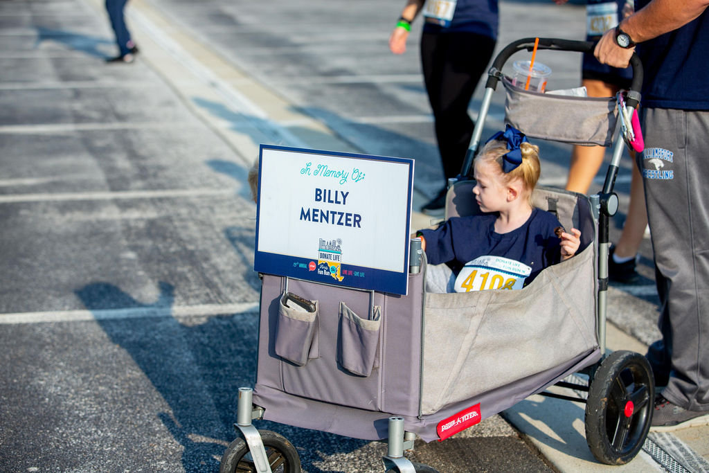 A young child is pushed in a wagon with a sign to honor Billy Mentzer's legacy at Infinite Legacy's Annual Donate Life Family Fun Run.