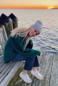 Catherine Pratt, a donor hero sits on a bench by the ocean during sunset.