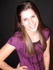 Taylor Storch, donor hero wears a purple shirt and smiles into the camera.