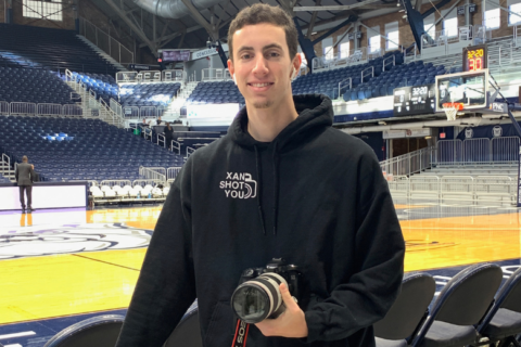 Xan Korman at the Butler University basketball courts holding his camera.