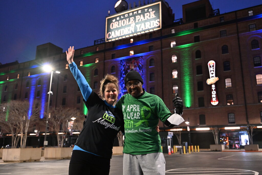 Volunteers wear Donate Life apparel in front of a brightly lit Camden Yards during Donate Life Month.