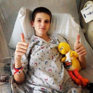 Pediatric heart recipient Brandon Kerrigan lies in his hospital bed, holding a Big Bird stuffed animal and gives a thumb-up.
