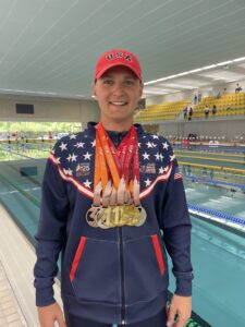 Heart recipient Brandon Kerrigan stands in front of an Olympic swimming pool and proudly wears the medals he earned while swimming for Team USA at the World Transplant Games.