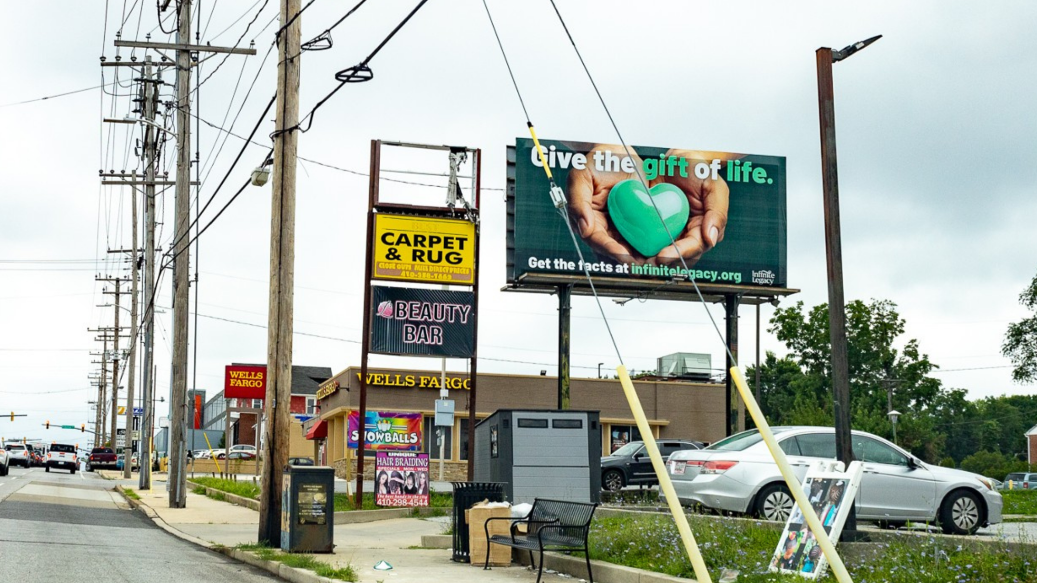 Urban street scene with utility poles and a large billboard that reads 'Give the gift of life' and shows a green heart held by hands (outdoor ad).