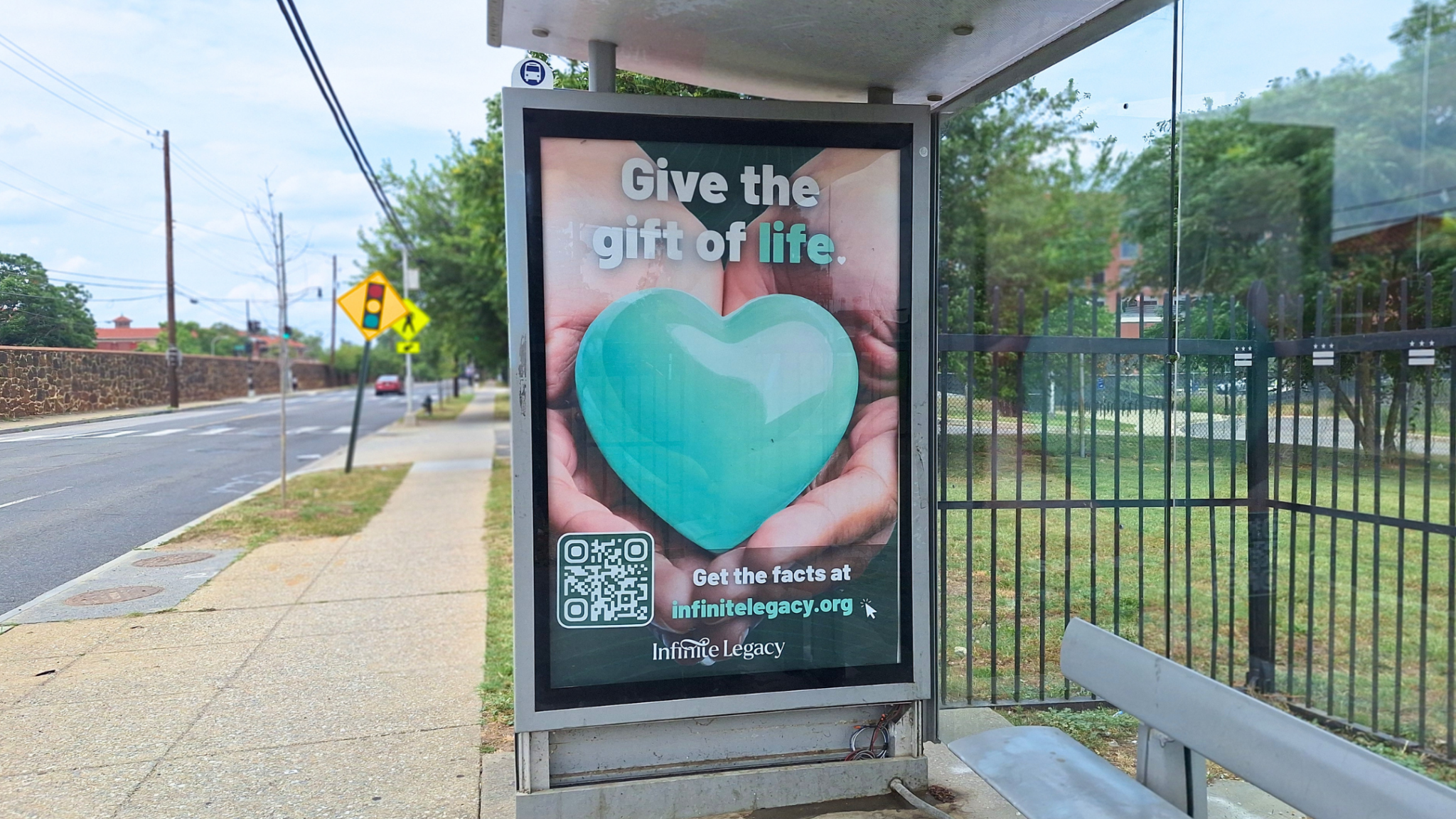 Bus-stop poster promoting organ donation: teal heart cupped in hands with the words 'Give the gift of life' and a QR code at the bottom.