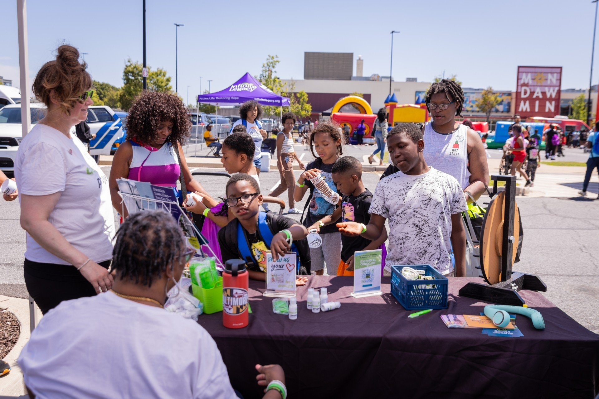 Community health fair booth with kids and volunteers gathered around a table of freebies and information.